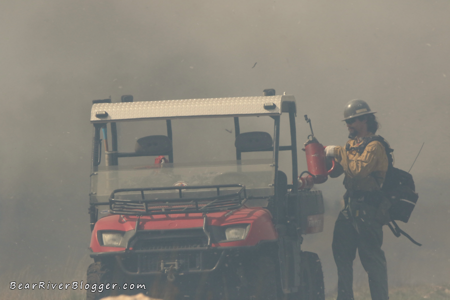 firefighter getting a drip can on the bear river migratory bird refuge with a lot of smoke in the background
